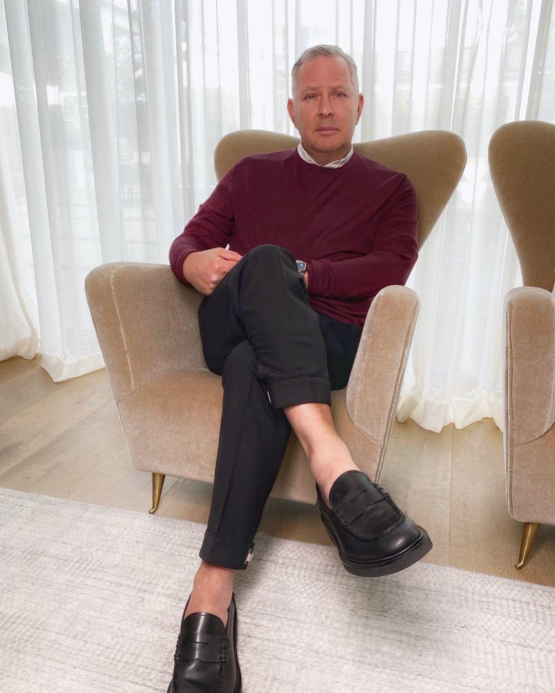 A photo of PK Kemsley in a red sweater and black pant, sitting on a couch.
