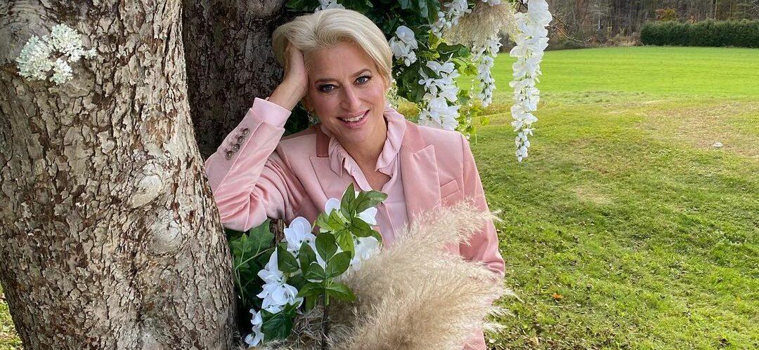 A photo of Dorinda Medley in a pink outfit, leaning against a huge tree in a green field.