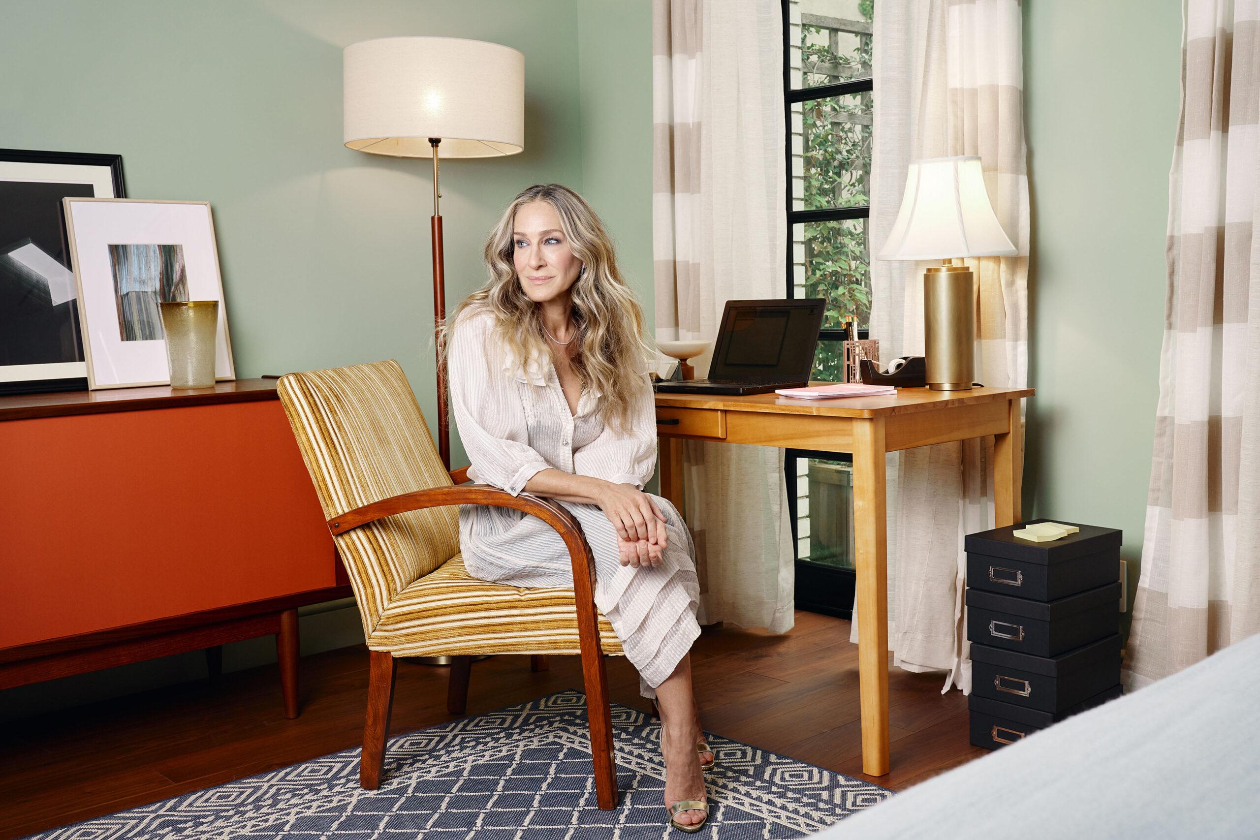 Sarah Jessica Parker sitting in Carrie Bradshaws' iconic New York City apartment