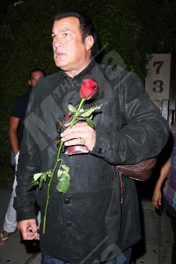 A photo showing Steven Seagal in a black outfit, holding a single red rose.