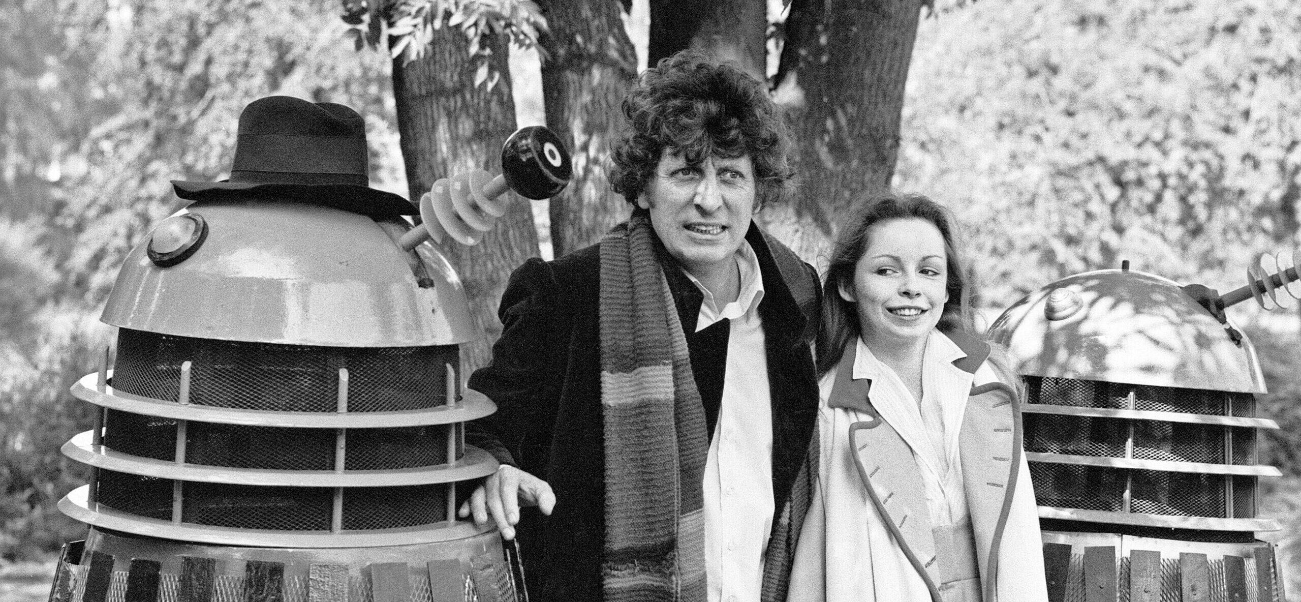 Tom Baker poses as the Fourth Doctor in Doctor Who next to a Dalek and Sarah Baker