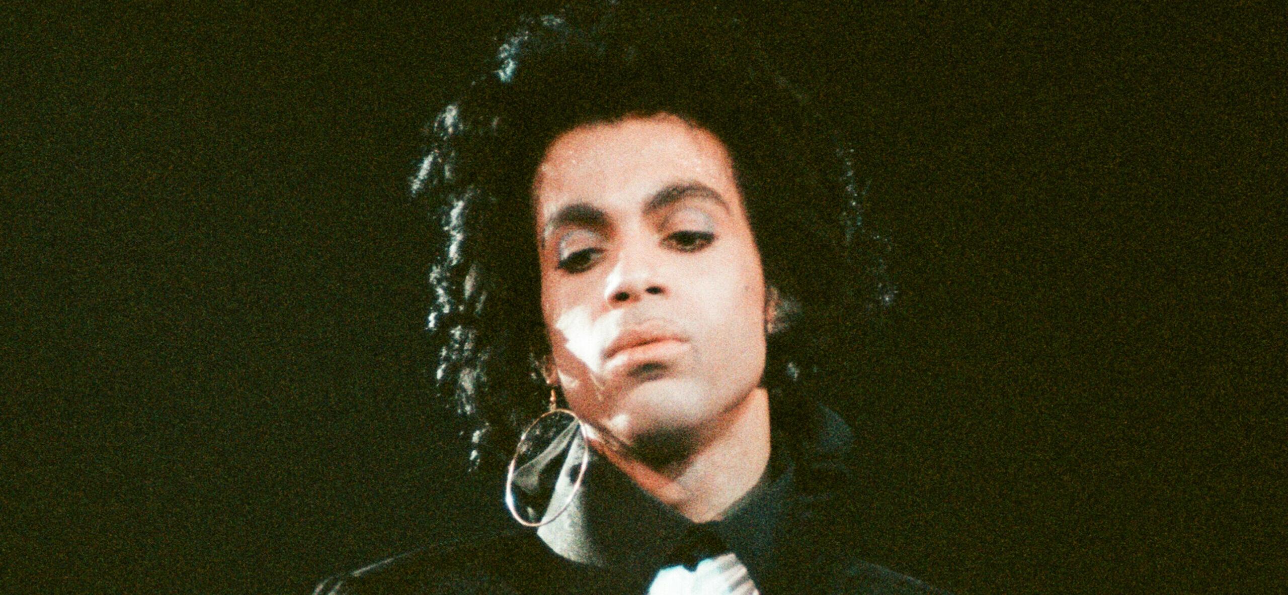 Prince in a black long-sleeve T-shirt with a white scarf around his neck.