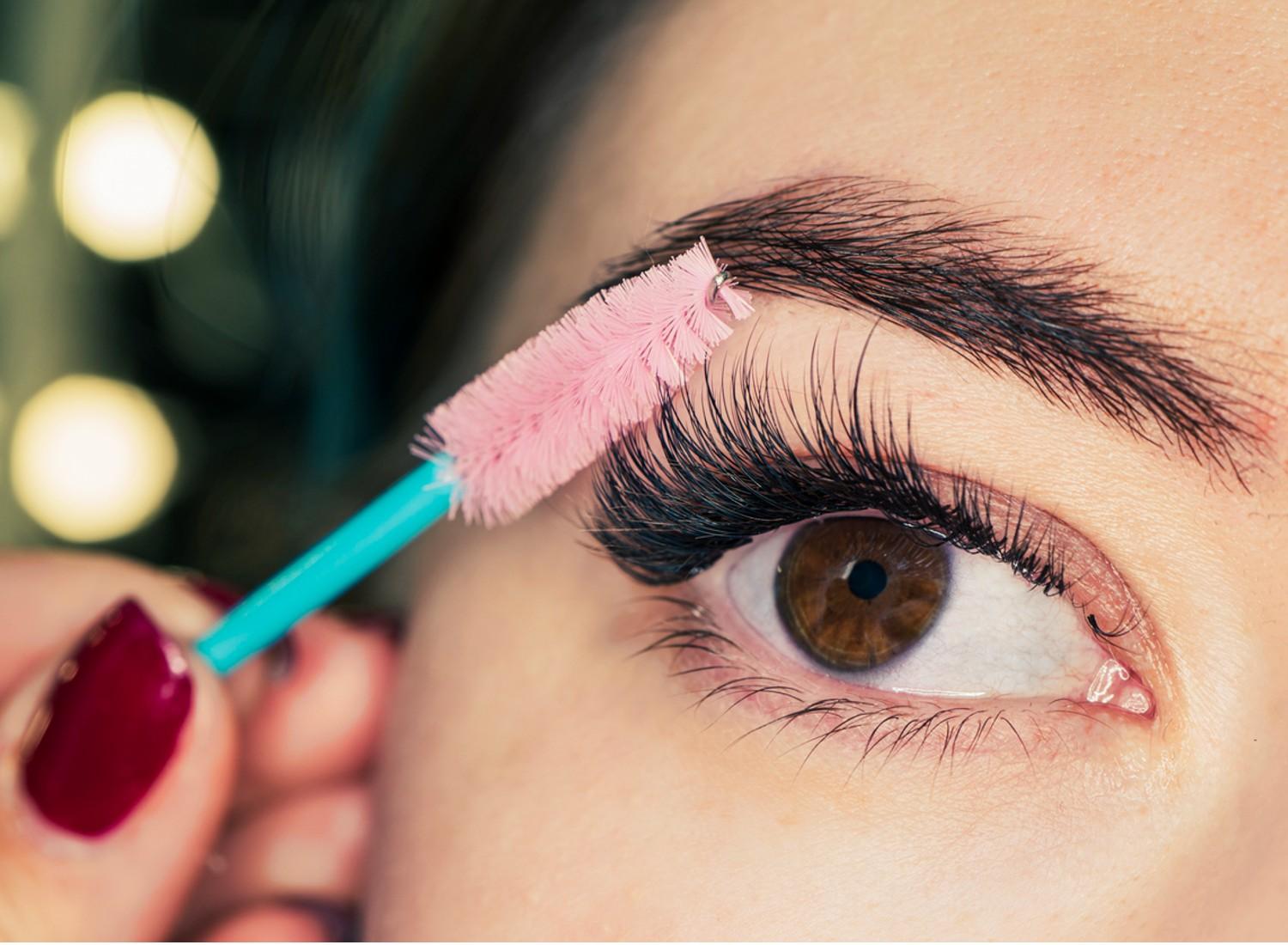 A woman applying mascara to her lashes.