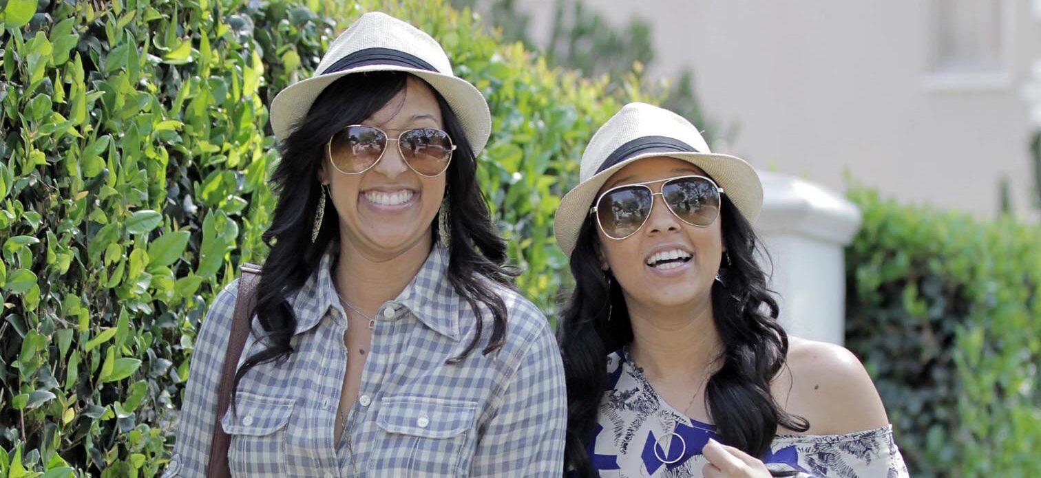 TIA AND TAMERA MOWRY SMILING AND HOLDING HANDS