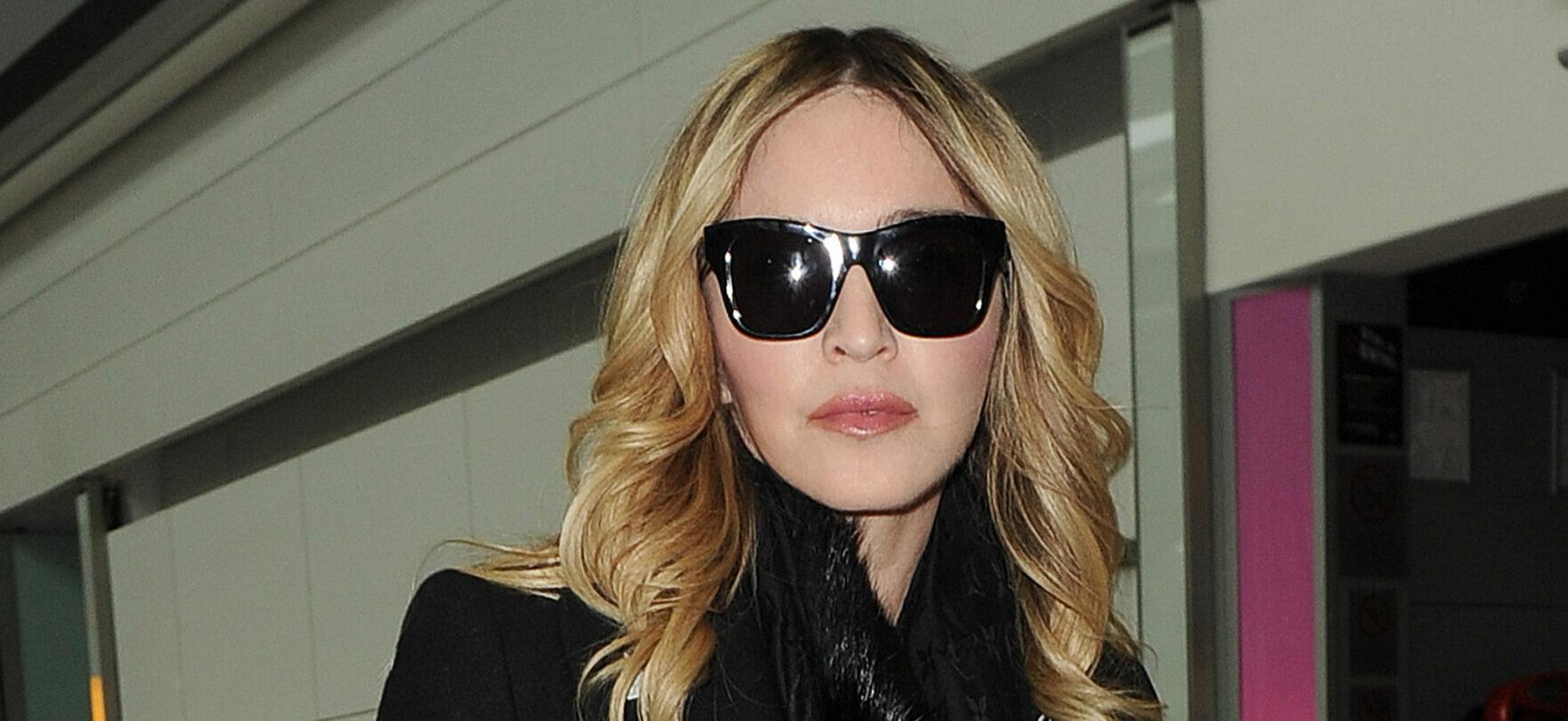 Madonna arriving at Heathrow Airport. She wore sunglasses and an all black outfit, with a fur coat, polkadot trousers and a black Gucci Ghost x Alessandro Michele tote handbag