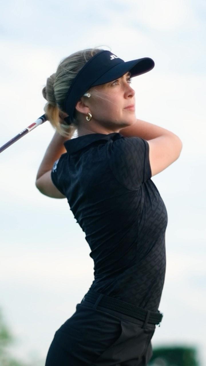Grace Charis plays golf in a black polo top and shorts