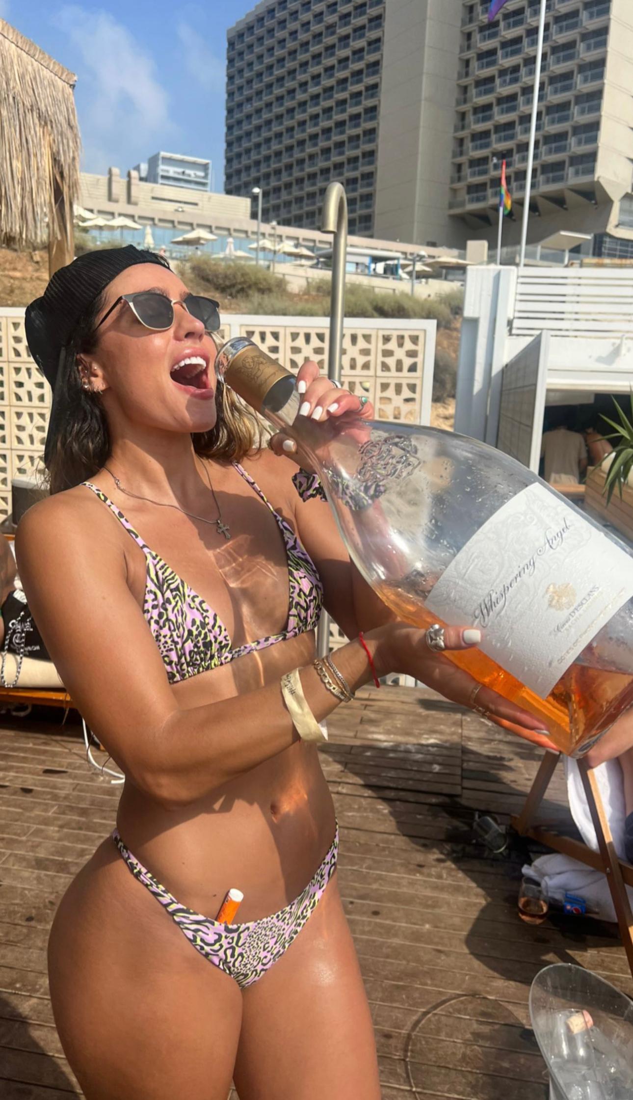 Somer Ray segurando uma grande garrafa de vinho enquanto usava um pequeno biquíni.