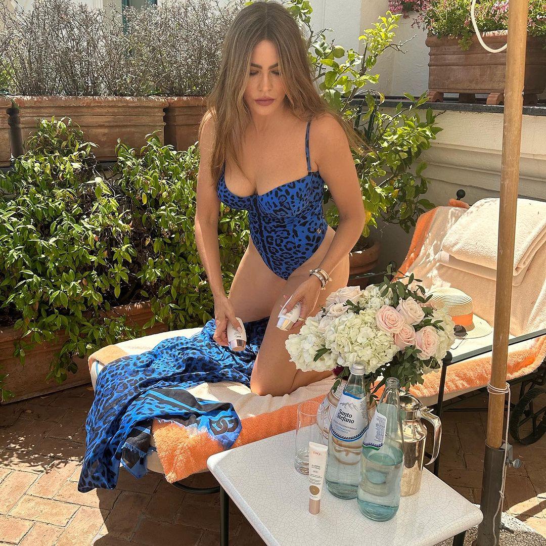Sofia Vergara wearing a spotty blue swimsuit and kneeling on a sun bed while in Italy.