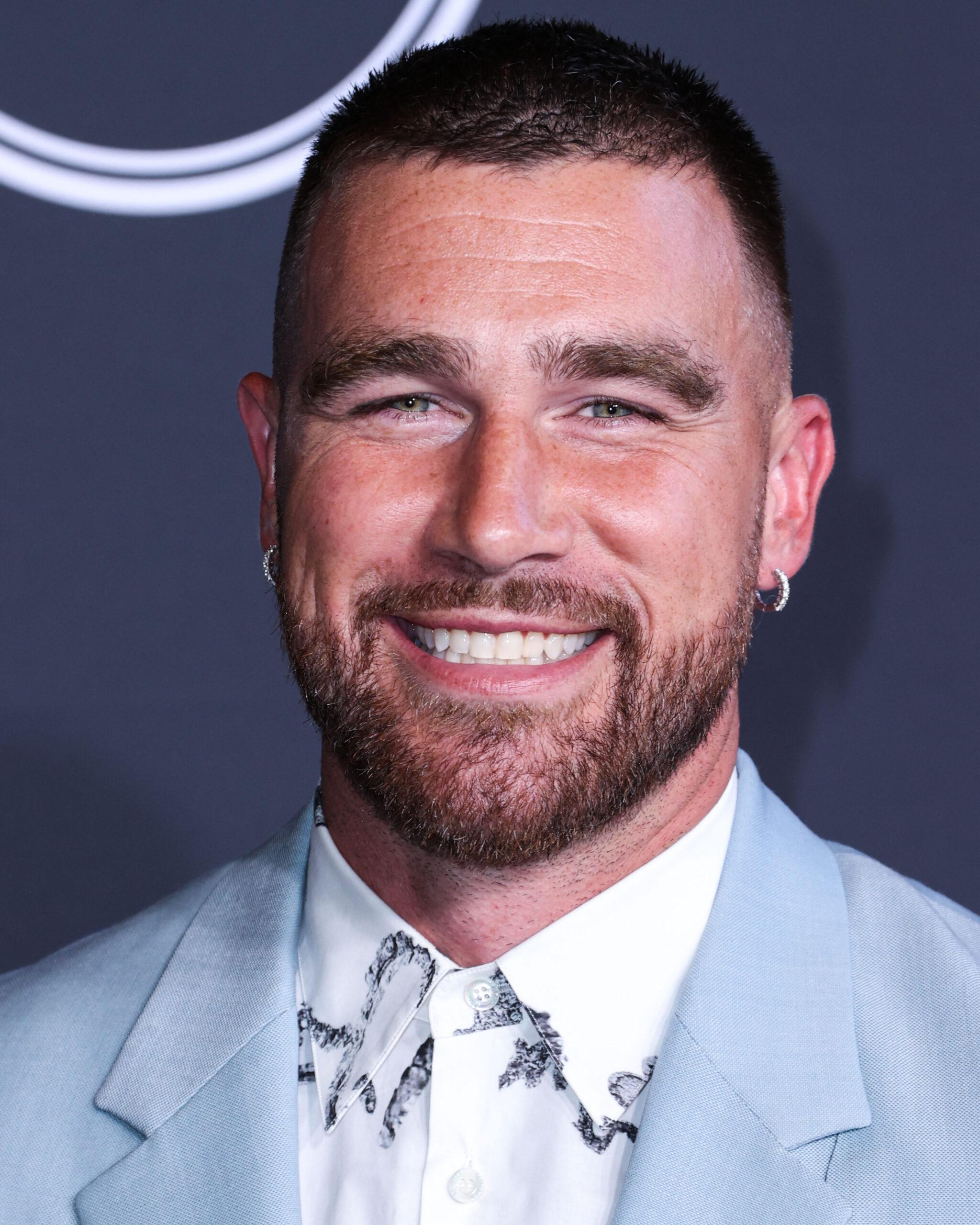 Travis Kelce wears a light blue suit while smiling for the camera