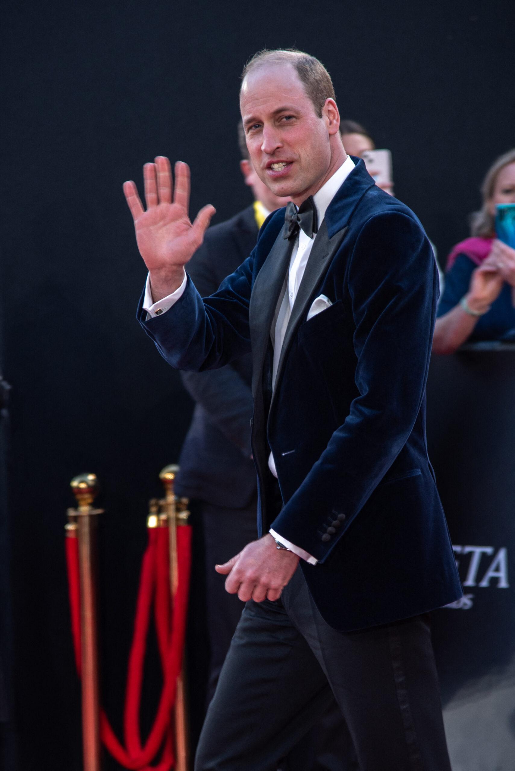Prince William wearing a suit waves his right hand.