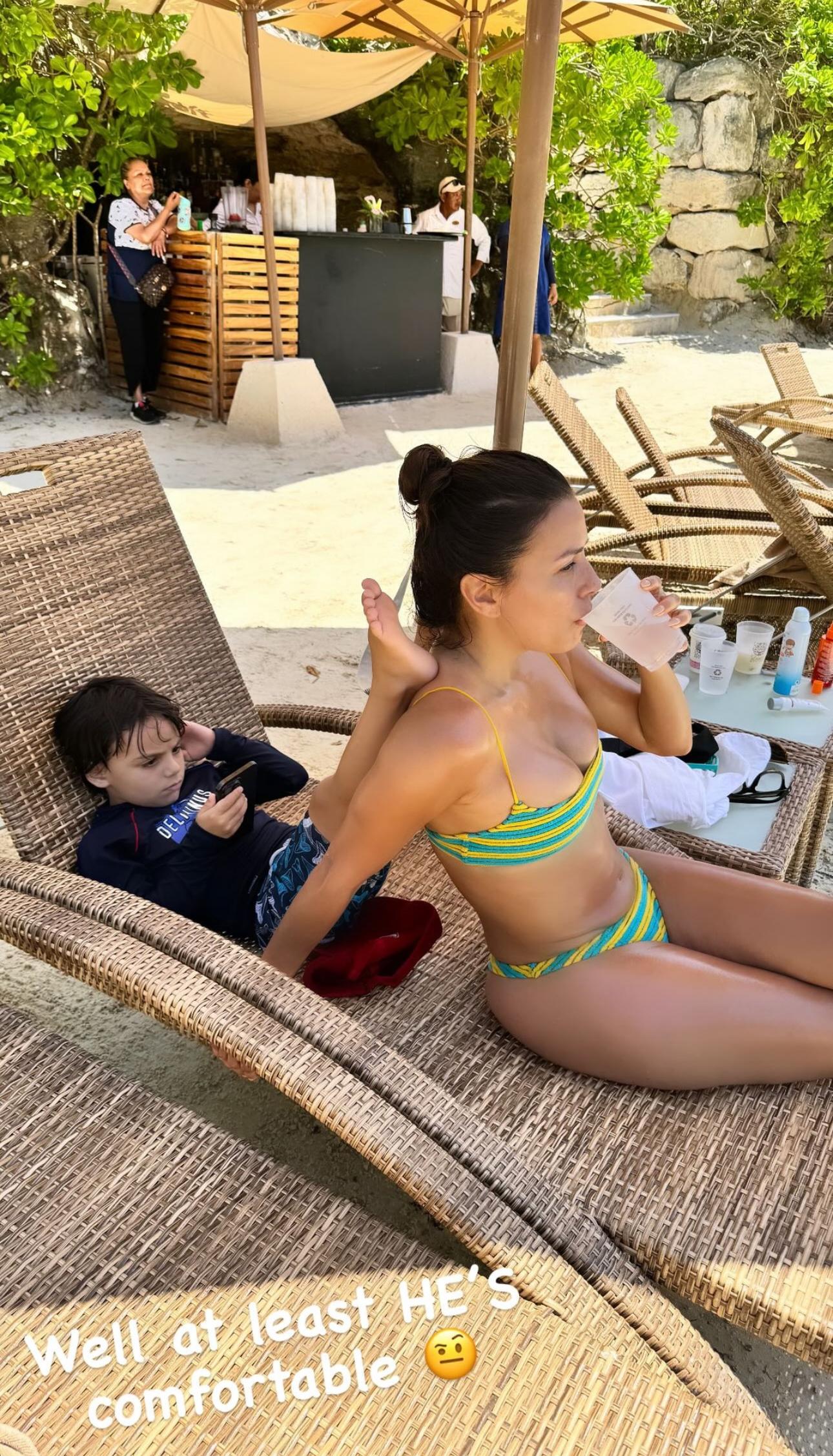 Eva Longoria toma uma bebida enquanto o filho pendura as pernas nas costas dela.