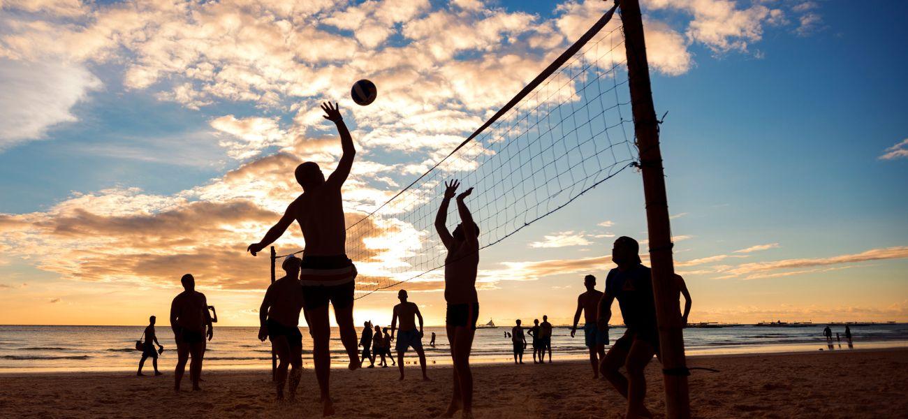 People playing beach volleyball at sunset