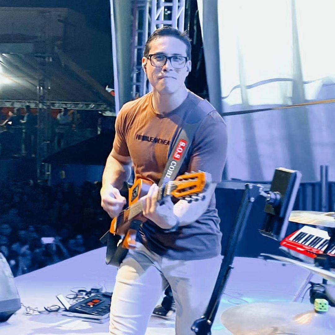 Ayres Sasaki smiles while playing guitar