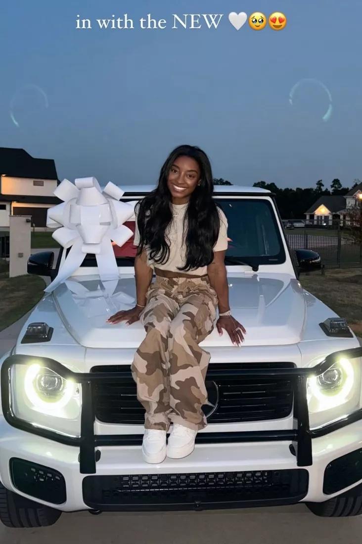 Simone Biles sentada no capô de seu novo G-Wagon branco