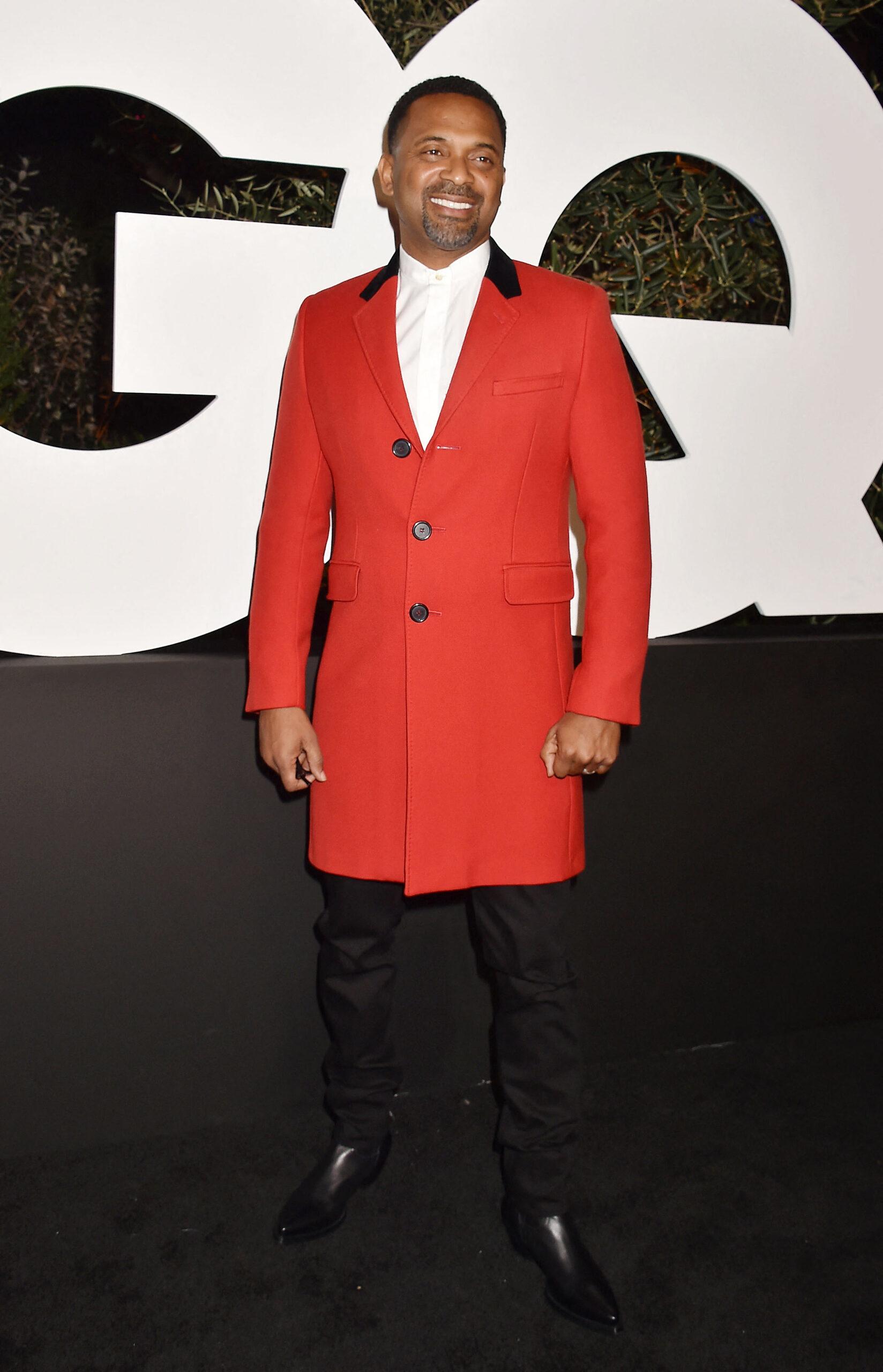 Mike EPPS poses in a red jacket on a red car.