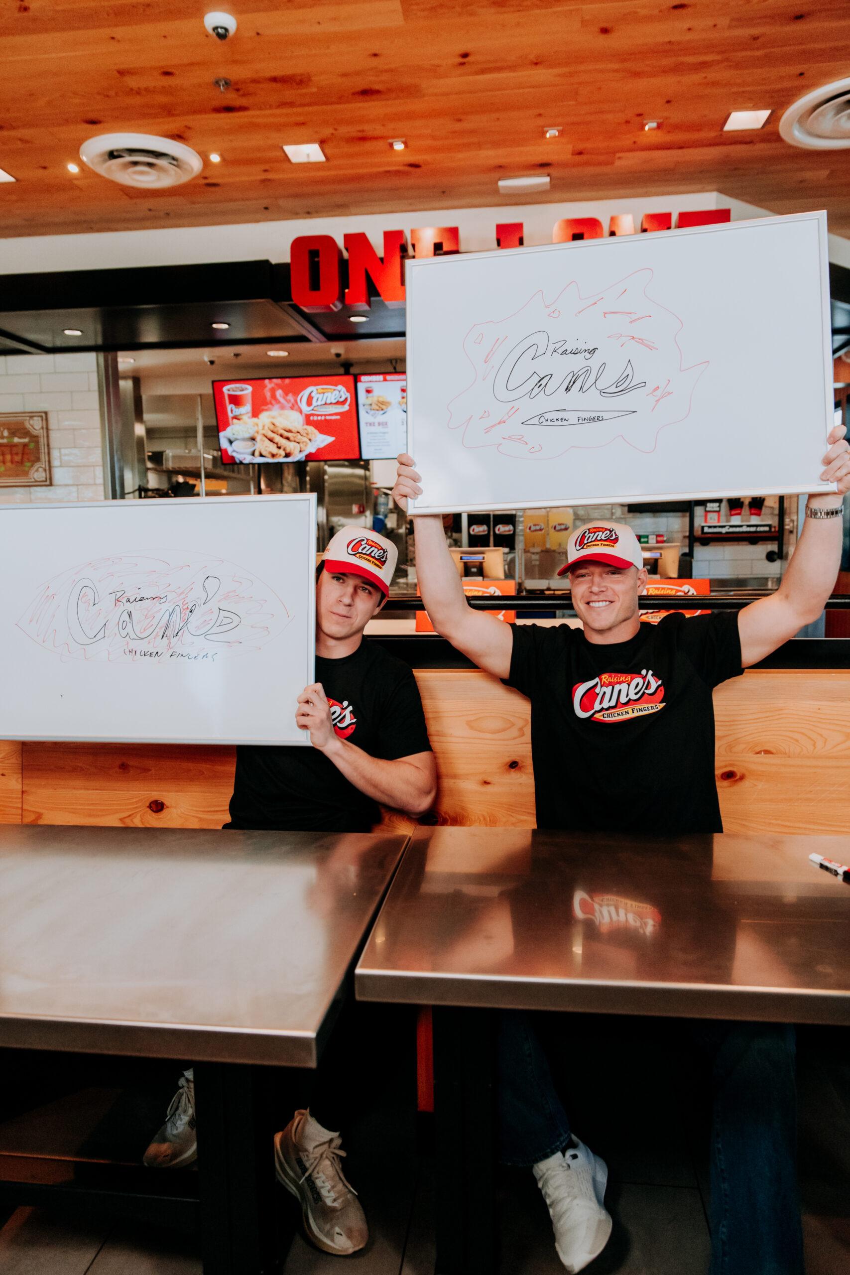 Christian and Luke McCaffrey holding up white boards with Raising Cane's logos