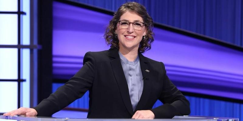 A lovely photo of Mayim Bialik in a black suit and purple inner blouse.