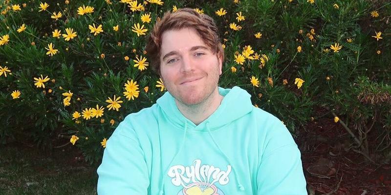 A photo of Shane Dawson in a hoodie, sitting beside a bed of yellow flowers