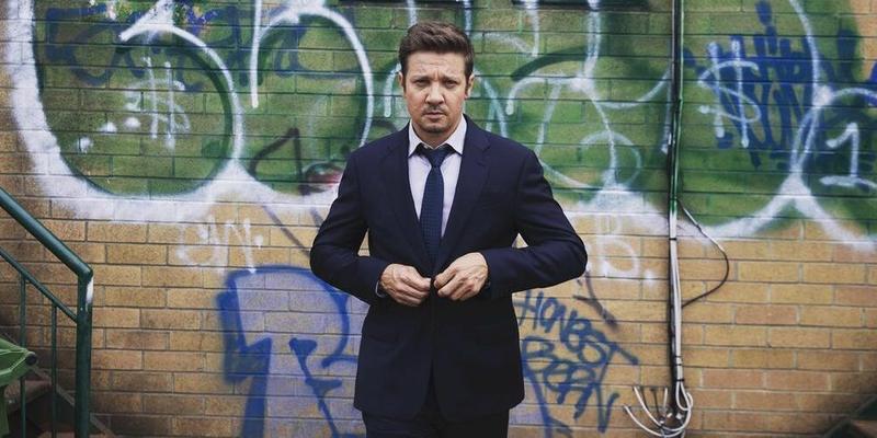 A photo showing Jeremy Renner in a black suit and pant, with a tie to match.