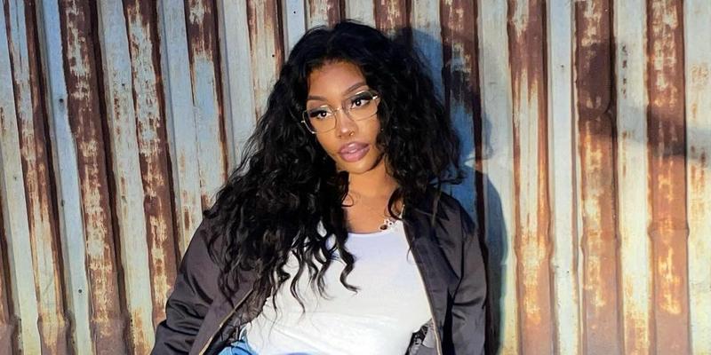 A photo showing SZA rocking a black jacket over a white shirt and denim pant.