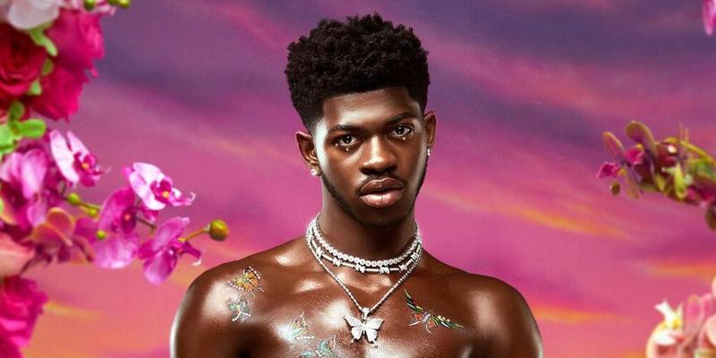 A photo showing bare-chested Lil Nas X in a garden filled with colorful flowers.