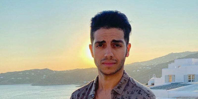 Mena Massoud poses in front of a sunset while in Greece.