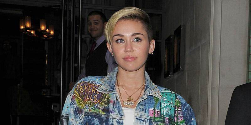 Miley Cyrus leaves her hotel arm in arm with her bodyguard The singer was wearing a white crop top black knee high boots denim hot pants and a matching denim jacket