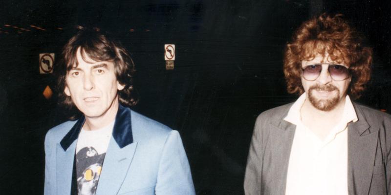 George Harrison and Jeff Lynne in blue and brown suits respectively at an event.