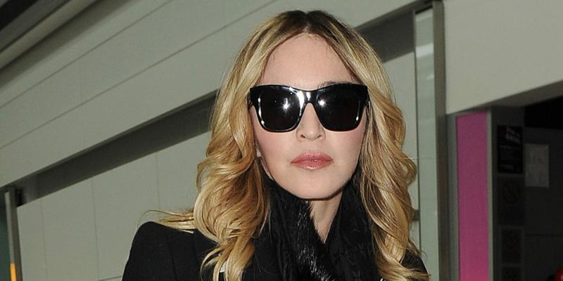 Madonna arriving at Heathrow Airport. She wore sunglasses and an all black outfit, with a fur coat, polkadot trousers and a black Gucci Ghost x Alessandro Michele tote handbag