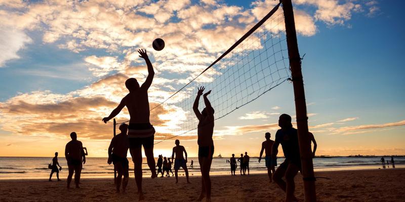 People playing beach volleyball at sunset