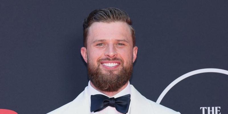 Harrison Butker smiling in a white suit on the red carpet.