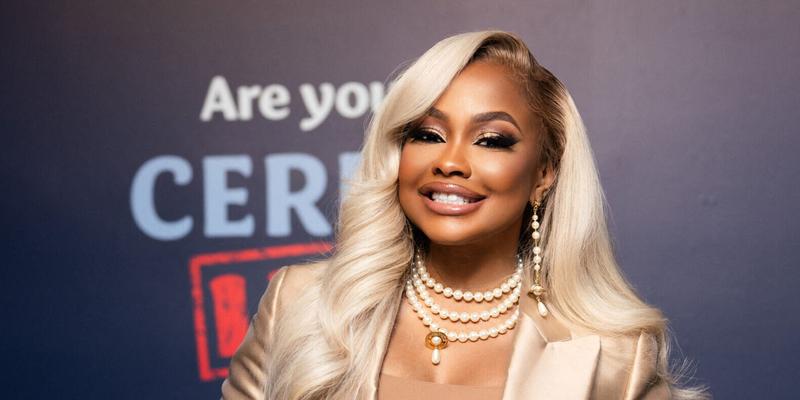 Phaedra Parks posing in a gold suit with blonde hair smiling for a picture.